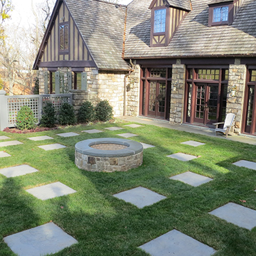 Enclosed yard behind a stone house with placed pavers and a central water feature