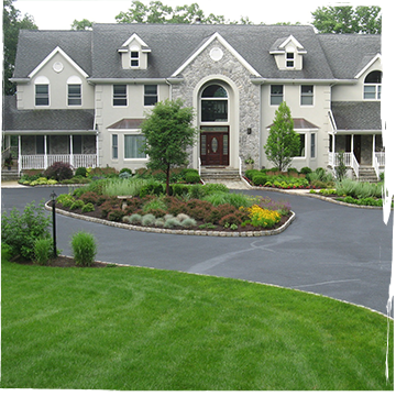 Circle driveway with a landscaped island of a tree and flowering bushes in front of a grey house